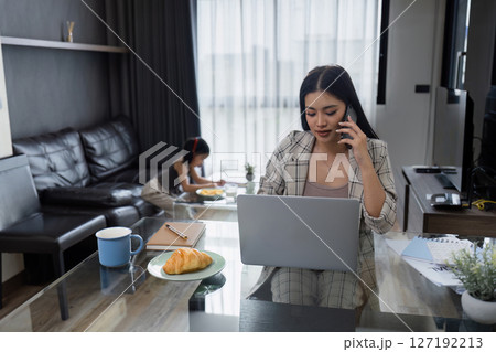 Business woman working at home. working woman talk on mobile and working on laptop and take care of her daughter during summer 127192213