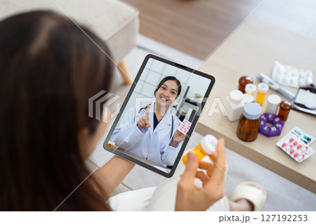 Senior Asian woman video calling with doctor on tablet, consultation health issues and medication online. Doctor concept of telemedicine Senior Asian woman video calling with doctor on tablet, consultation health issues and medication online. Doctor concept of telemedicine 127192253