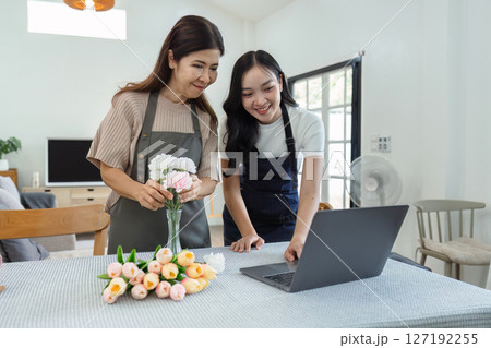 mother and daughter arrange flowers together as a hobby. mother and daughter spend free time doing flower arranging activities together and looking at laptop mother and daughter arrange flowers together as a hobby. mother and daughter spend free time doing flower arranging activities together and looking at laptop 127192255