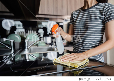 Young housewife wearing rubber protective gloves standing in cozy kitchen, cleaning table, using rag and effective detergent product. Household, cleaning service, housework, housewife concept Young housewife wearing rubber protective gloves standing in cozy kitchen, cleaning table, using rag and effective detergent product. Household, cleaning service, housework, housewife concept 127192293