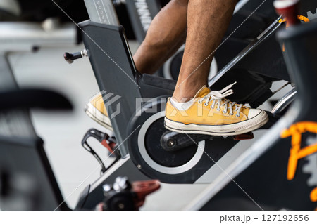 Workout on Spinner Bike. Close-up of a person exercising on a stationary bike with bright sneakers. 127192656