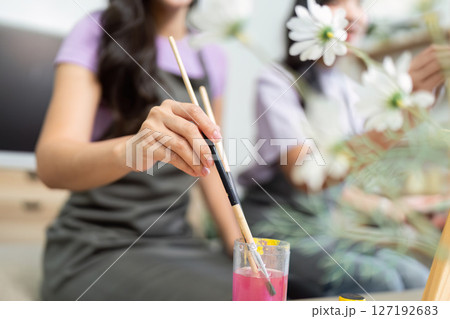 Couple Painting Together. Two young women enjoying a creative moment while painting in a cozy indoor setting. Couple Painting Together. Two young women enjoying a creative moment while painting in a cozy indoor setting. 127192683
