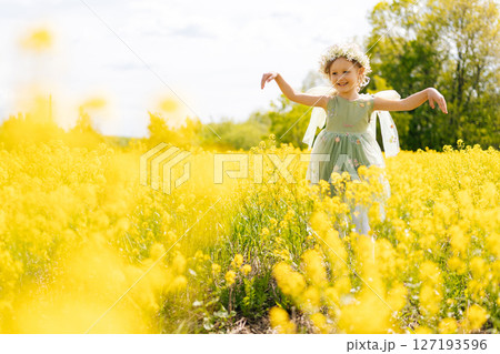 Happy preschooler girl wearing vibrant flower crown and fairy green dress, joyfully playing in sunny field filled with blooming yellow flowers in bright summer day. Concept of happiness childhood Happy preschooler girl wearing vibrant flower crown and fairy green dress, joyfully playing in sunny field filled with blooming yellow flowers in bright summer day. Concept of happiness childhood 127193596