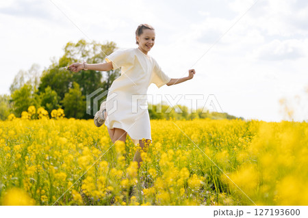 Happy little girl in white dress running joyfully through vibrant field of yellow flowers, embracing warmth of sunny summer day reveling in nature beauty and freedom. Concept of outdoor recreation. Happy little girl in white dress running joyfully through vibrant field of yellow flowers, embracing warmth of sunny summer day reveling in nature beauty and freedom. Concept of outdoor recreation. 127193600
