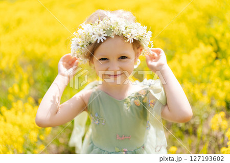 Portrait of adorable child girl in beautiful flower crown and fairy dress playing in blooming yellow meadow on sunny summer day, enjoying warm weather and vibrant colors of nature, looking at camera. Portrait of adorable child girl in beautiful flower crown and fairy dress playing in blooming yellow meadow on sunny summer day, enjoying warm weather and vibrant colors of nature, looking at camera. 127193602