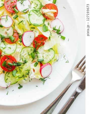 Plate with fresh spring salad of sliced radish, cherry tomatoes, cucumber, greens and iceberg salad covered in olive oil, top view of plate with vitamin meal. Plate with fresh spring salad of sliced radish, cherry tomatoes, cucumber, greens and iceberg salad covered in olive oil, top view of plate with vitamin meal. 127193673