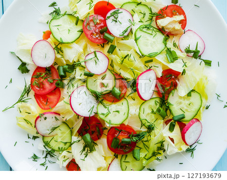 Plate with fresh spring salad of sliced radish, cherry tomatoes, cucumber, greens and iceberg salad covered in olive oil, top view of plate with vitamin meal. Plate with fresh spring salad of sliced radish, cherry tomatoes, cucumber, greens and iceberg salad covered in olive oil, top view of plate with vitamin meal. 127193679