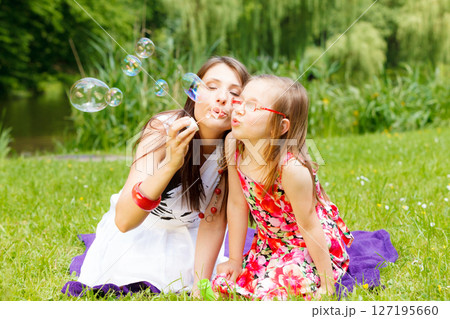 Mother and little girl blowing soap bubbles in park. 127195660