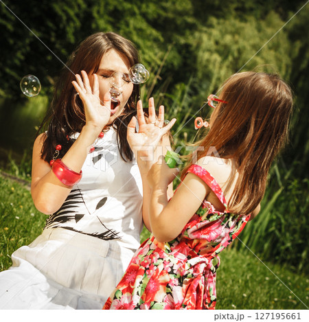 Mother and little girl blowing soap bubbles in park. 127195661