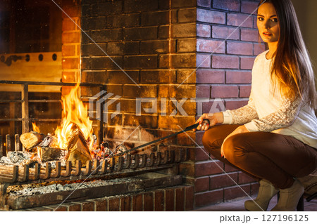 Woman with fire iron poker at home fireplace. 127196125