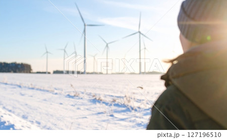 Woman near a wind turbine in a snowy winter landscape, symbolizing renewable energy and green technology 127196510