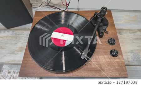 Wooden vinyl record player with black record in operation, on light background. 127197038