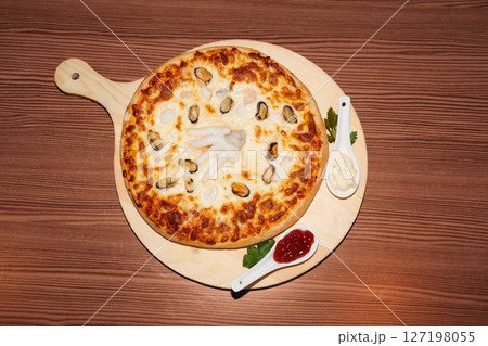 Seafood pizza and sauces on wooden background. Delicious freshly prepared meal, perfect for menus, restaurants, or food delivery concepts. Seafood pizza and sauces on wooden background. Delicious freshly prepared meal, perfect for menus, restaurants, or food delivery concepts. 127198055