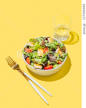 Vegetable salad with lettuce, tomatoes, croutons and olives in a bowl on a yellow background 127200495