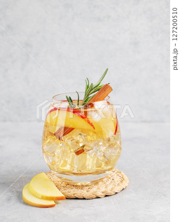 Apple cocktail or cider with ice, garnished with cinnamon and rosemary in a glass Apple cocktail or cider with ice, garnished with cinnamon and rosemary in a glass 127200510
