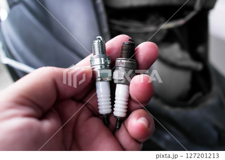 A hand holds two spark plugs comparison, one new and one used A hand holds two spark plugs comparison, one new and one used 127201213