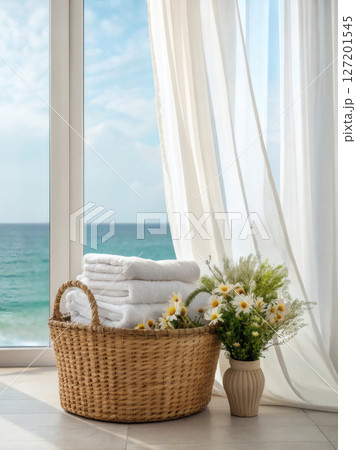 Wicker basket with towels and flowers near window with ocean view and curtains. 127201545