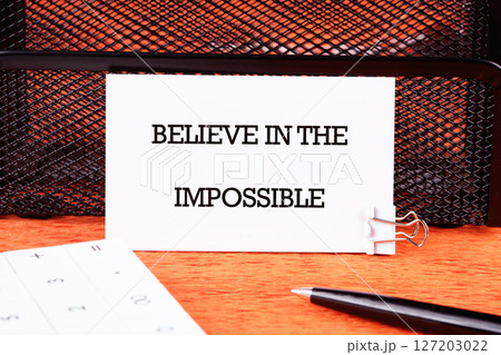 Motivational quote. BELIEVE IN THE IMPOSSIBLE text written on a business card next to a pen and a calculator in a prominent place 127203022