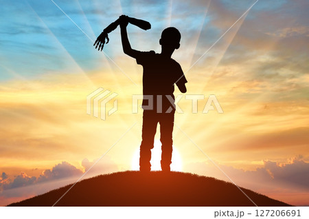 Silhouette of a disabled child standing on a hill at sunset, proudly holding a prosthetic arm 127206691