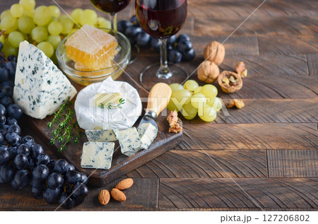 Cheese plate with grapes, honey, nuts and red wine on a wooden table, toned image. Cheese plate with grapes, honey, nuts and red wine on a wooden table, toned image. 127206802
