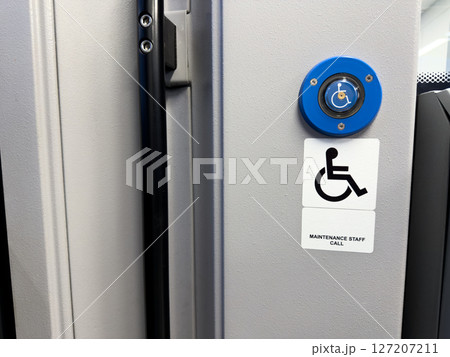 Modern accessibility assistance button with blue wheelchair symbol and maintenance staff call sign mounted on light gray wall inside public transportation, symbolizing inclusive design 127207211