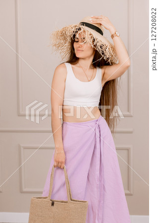 Attractive woman in summer outfit with straw hat and jute bag, perfect for vacation, beach or boho fashion shoots. 127208022