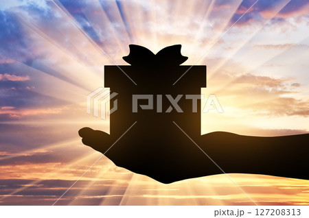 Altruism. Silhouette of a hand giving a gift on a sunset background 127208313