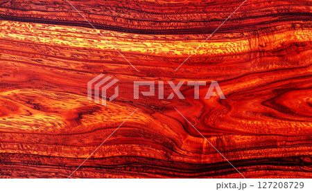 wood texture background, mahogany wood texture, showcasing its rich reddish brown color and seamless grain pattern. This luxurious wood surface features elegant, swirling natural lines 127208729