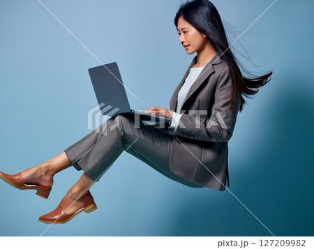 ノートPCを操作しながら空に浮いているスーツ姿の女性 127209982
