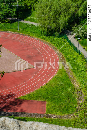 Curved red running track surrounded by grass and trees in summer. High quality photo 127210071