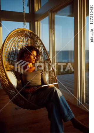 A woman is sitting in a wicker chair with a laptop in front of her A woman is sitting in a wicker chair with a laptop in front of her 127210439