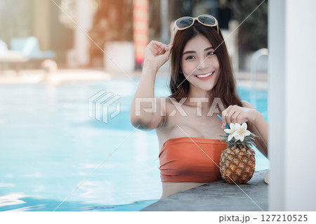 Sexy young asian woman in swimsuits in summer. beautiful woman in orange bikini with sunglasses and tropical drink in swimming pool. Sexy young asian woman in swimsuits in summer. beautiful woman in orange bikini with sunglasses and tropical drink in swimming pool. 127210525