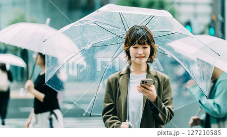 雨の中、傘をさしてスマホを使う女性（梅雨・6月） 127210585