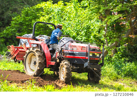 トラクターで畑を耕す若い男性 127210846