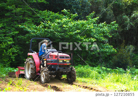 トラクターで畑を耕す若い男性 127210855