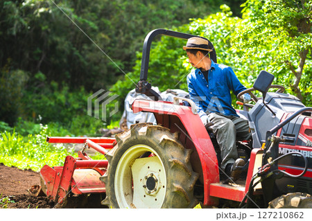 トラクターで畑を耕す若い男性 127210862