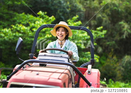 トラクターで畑を耕す女性 127210891