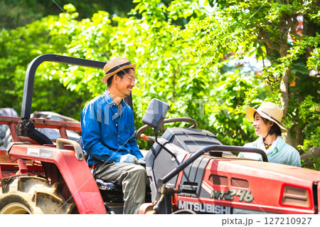 トラクターに乗る男性と見守る女性 127210927