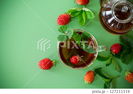 Bright strawberry tea in transparent glassware on a green background Bright strawberry tea in transparent glassware on a green background 127211319