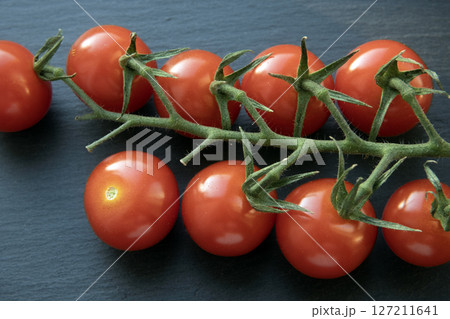 Red cherry tomatoes on a branch on gray background. Red cherry tomatoes on a branch on gray background. 127211641