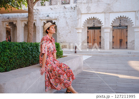 Young woman in an ethnic dress and hat exploring Al Seef Park in Dubai. Surrounded by traditional Emirati architecture and modern vibes, she enjoys the charm of Dubai Creek's cultural heritage. 127211995