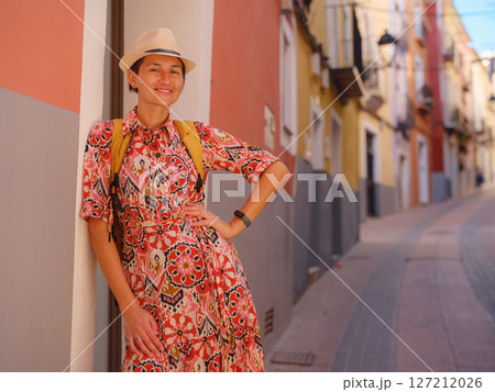Woman in dress strolls through colorful streets of Spanish coastal town of La Vila Joiosa or Villajoyosa. sunny winter atmosphere highlights charm of Mediterranean architecture and quiet seaside life 127212026