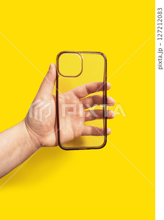 Hand holding a transparent smartphone case against a vibrant yellow background, showcasing modern design and functionality for mobile device protection and style enhancement Hand holding a transparent smartphone case against a vibrant yellow background, showcasing modern design and functionality for mobile device protection and style enhancement 127212083