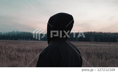 Dark landscape wiht guy. A Stylish Young Man in a black hoodie the Dusk Hours. Rear view. gloomy sunset. A dark forest, fog is spreading over the field. Dark landscape wiht guy. A Stylish Young Man in a black hoodie the Dusk Hours. Rear view. gloomy sunset. A dark forest, fog is spreading over the field. 127212189