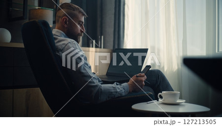 Financial Analyst Working on Laptop and Smartphone in Trading Software, Analyzing Real-Time Stocks 127213505