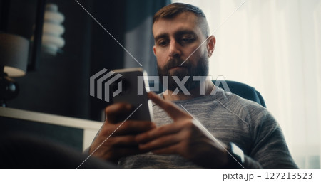 Stock Exchange Trader Analyzing Exchange Market Charts Using Smartphone in Cozy Office Stock Exchange Trader Analyzing Exchange Market Charts Using Smartphone in Cozy Office 127213523