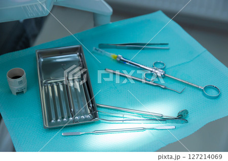 A Comprehensive Overview of Dental Instruments Arranged Neatly on a Blue Surgical Cloth in a Modern Dental Practice Setting with Bright Reflective Lighting 127214069