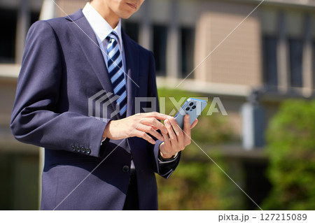 ビジネス街でスマートフォンを見るスーツの若いビジネスマン 127215089