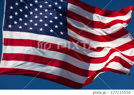 American Flag Waving In The Wind Against Deep Blue Sky. American Flag Waving In The Wind Against Deep Blue Sky. 127215550
