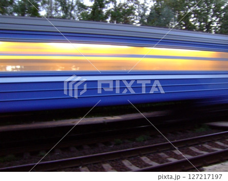 A train rushes past a station, showcasing its blue and yellow colors. The blurred effect emphasizes speed, while trees and tracks frame the travel experience at twilight. A train rushes past a station, showcasing its blue and yellow colors. The blurred effect emphasizes speed, while trees and tracks frame the travel experience at twilight. 127217197
